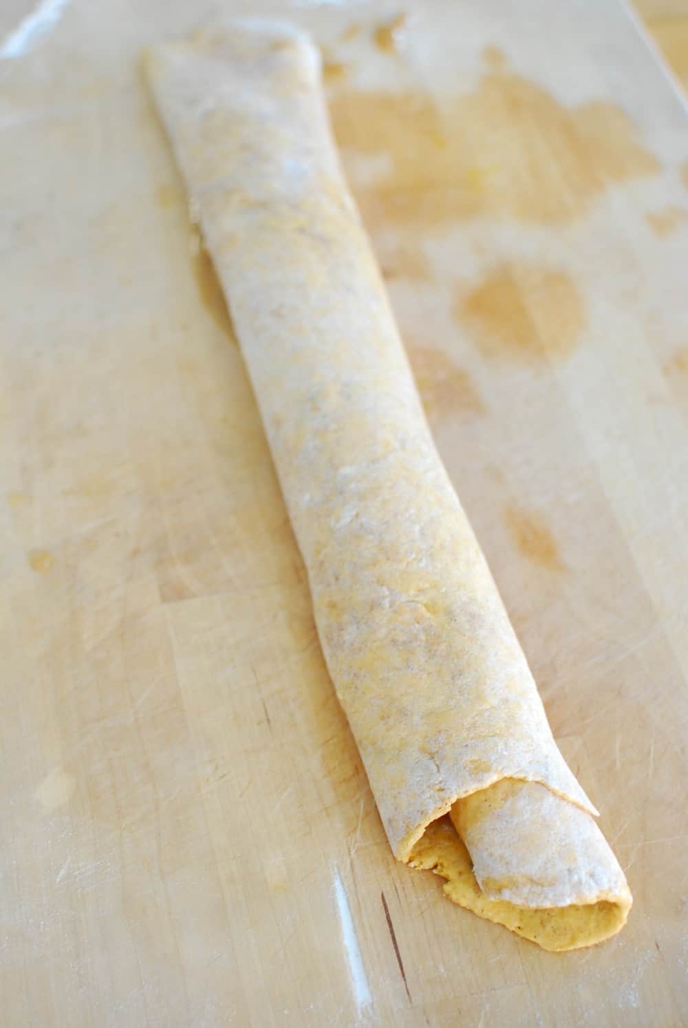 Rolled up pumpkin cinnamon dough on a cutting board