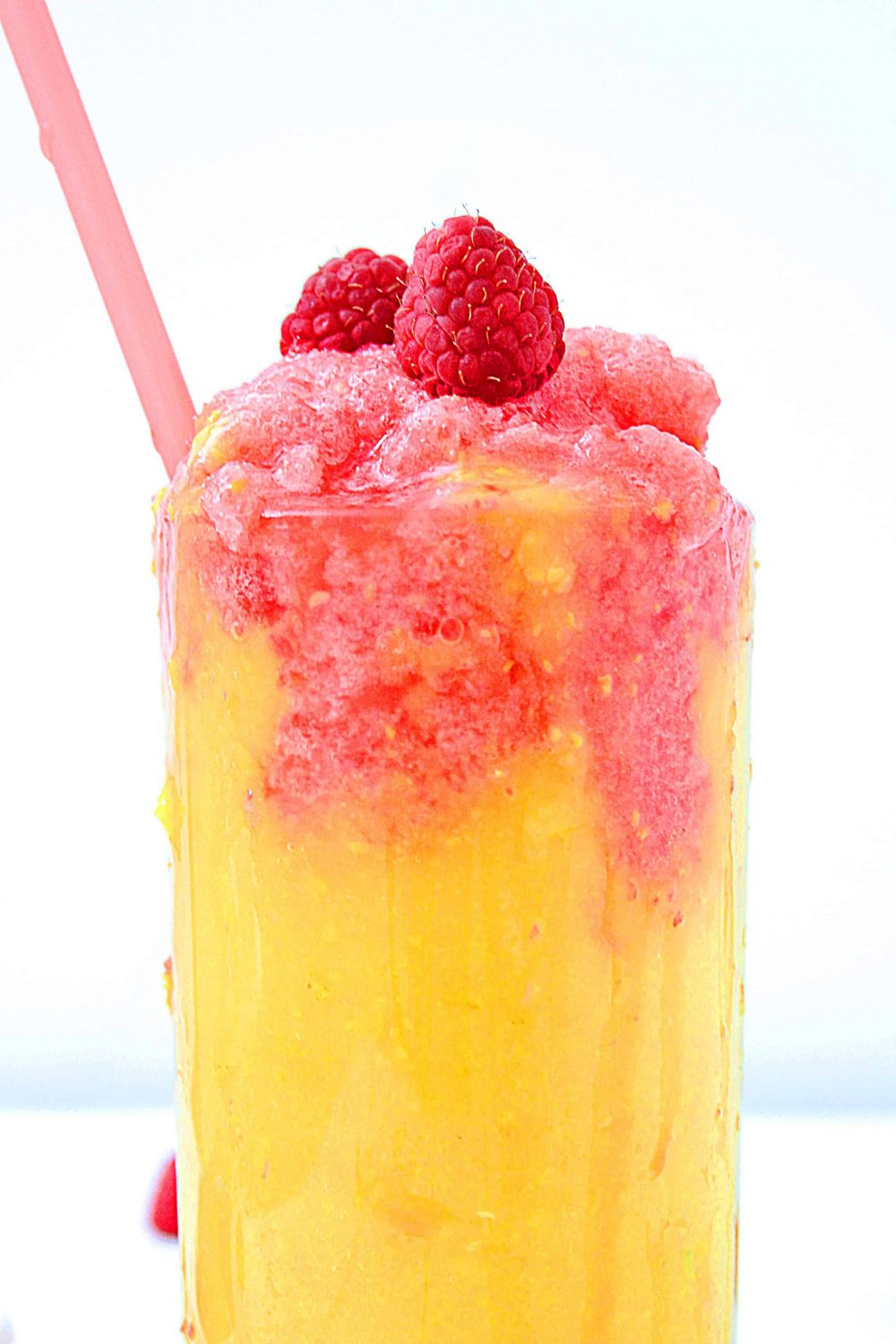 A glass full of mango raspberry smoothie with a pink straw