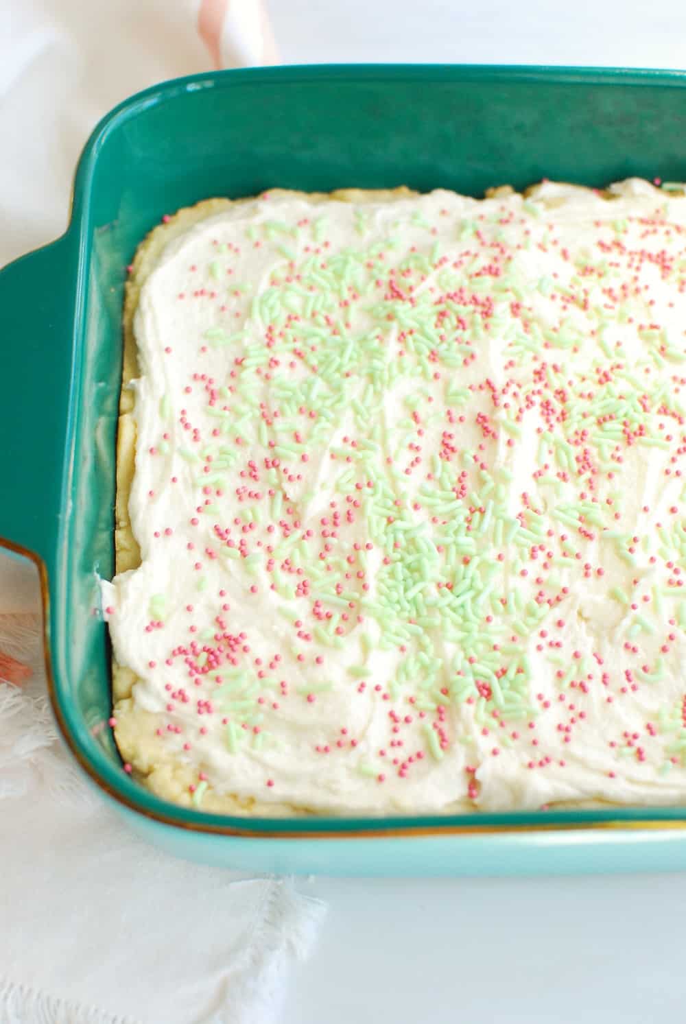 A pan full of sugar cookie bars topped with frosting and sprinkles