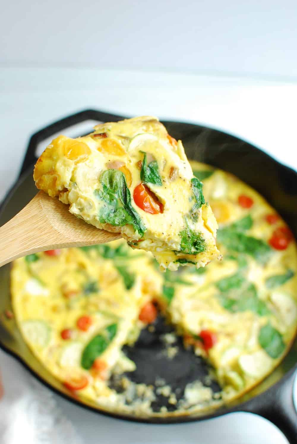 A wooden utensil holding a slice of frittata