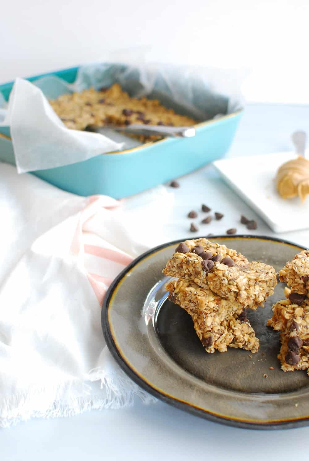 dairy free granola bars stacked on a plate, next to a pan of them