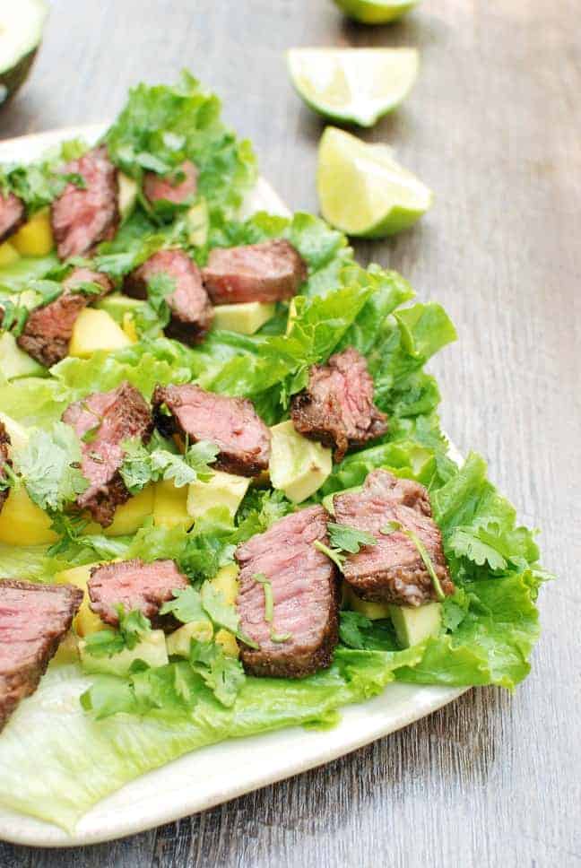 Steak lettuce wraps on a white plate next to a lime wedge