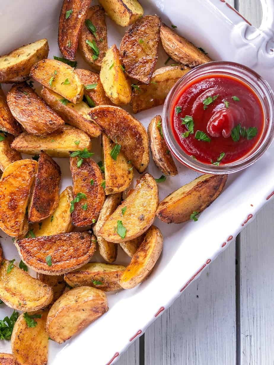 Baked Potato Wedges on a white platter next to sauce