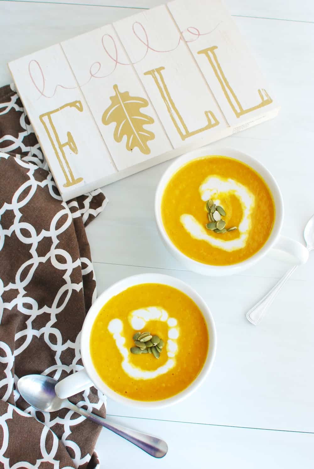 Two mugs full of vegan pumpkin soup next to a sign that says hello fall