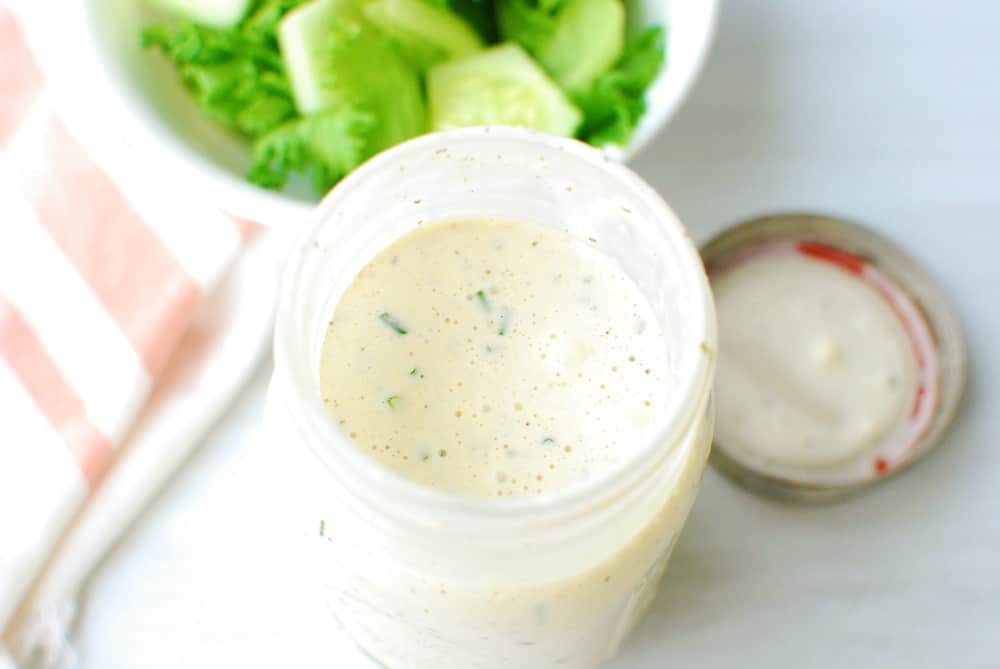 Dairy free ranch dressing in a mason jar next to a bowl of salad