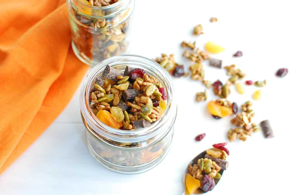 A jar of nut free trail mix with some spilled out on the table.