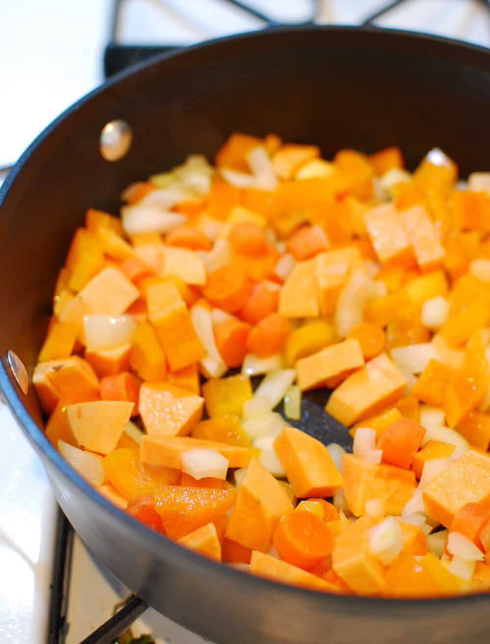 A pot with carrots, onions, pepper, and sweet potato sauteing in olive oil