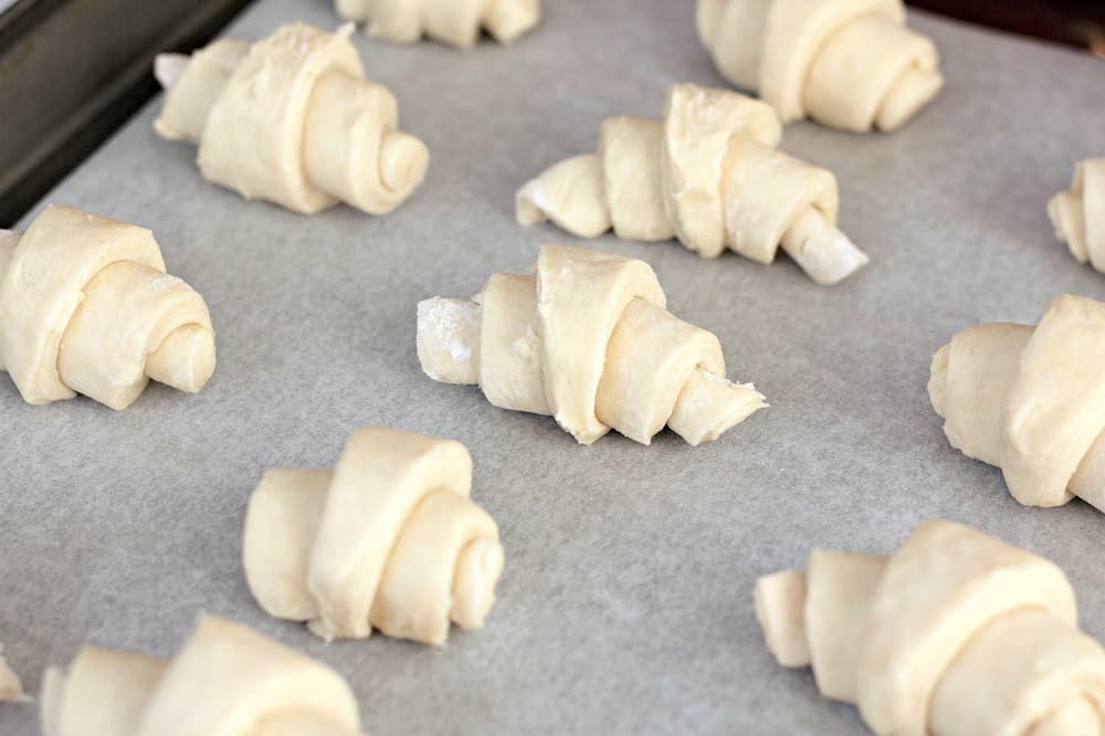Crescent rolls rolled up on a baking sheet with parchment paper
