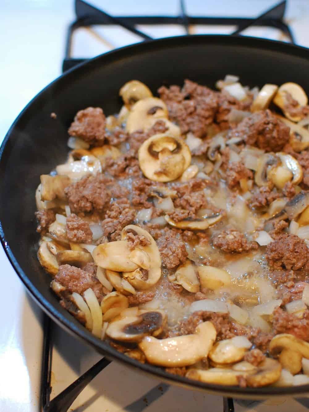 Beef simmering in a pan with mushrooms and onions