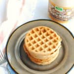 a stack of dairy free waffles on a plate next to a bottle of maple syrup