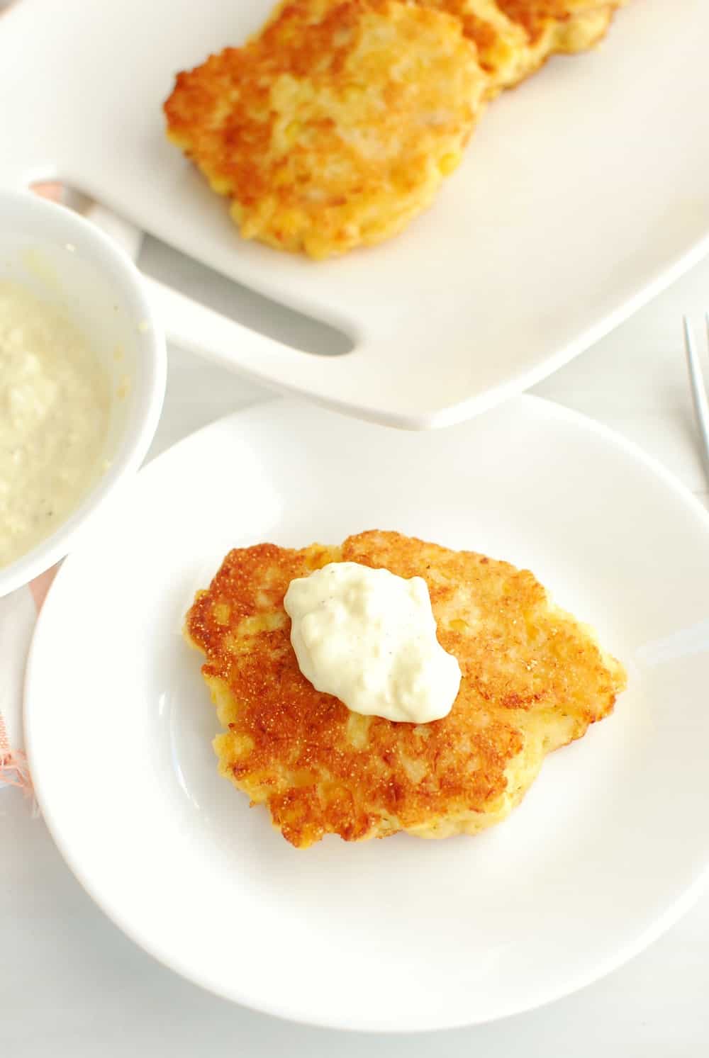 a salmon corn fritter on a white plate with a dollop of garlic mayo aioli