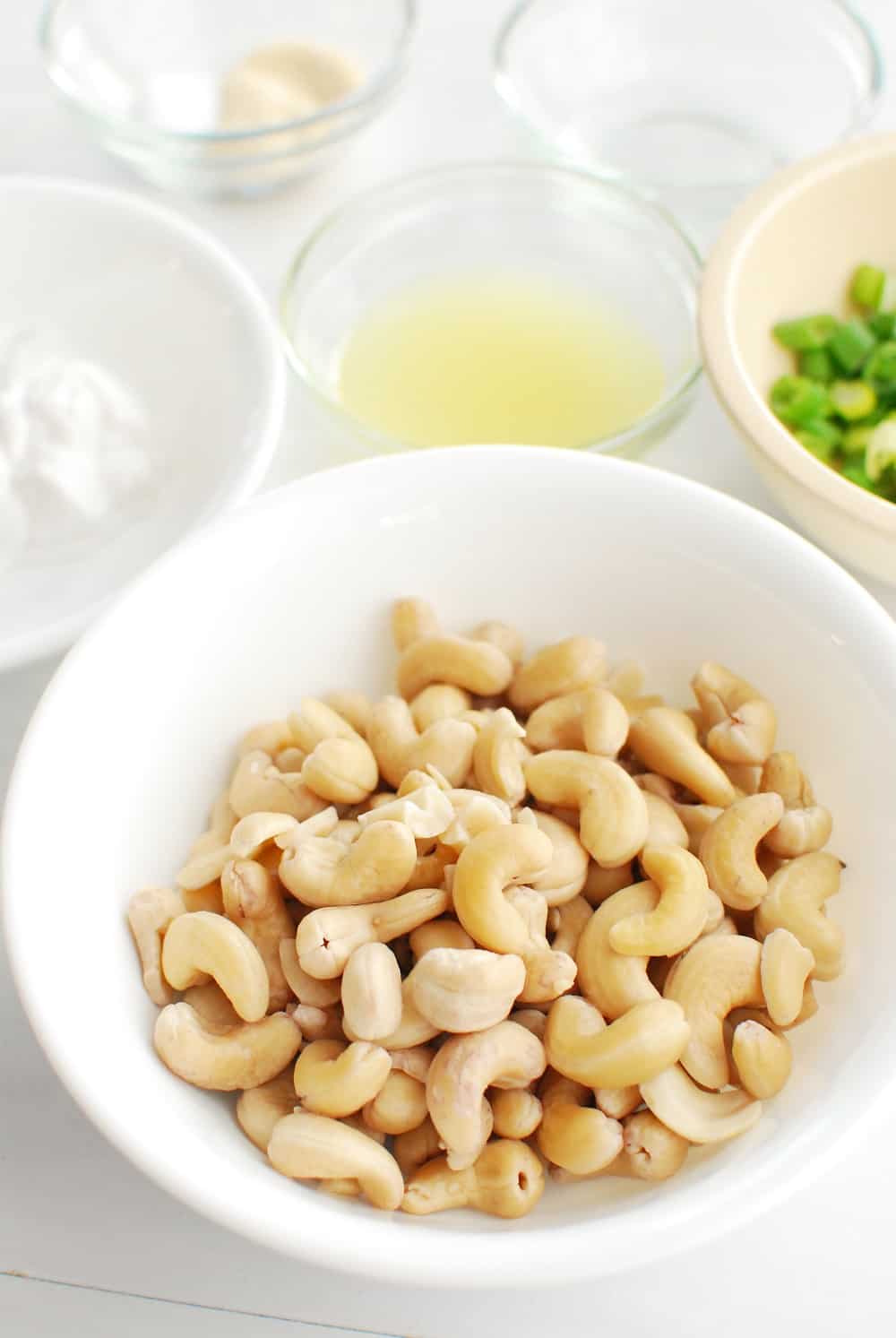 a bowl of soaked cashews next to some lemon juice, coconut cream, and scallions