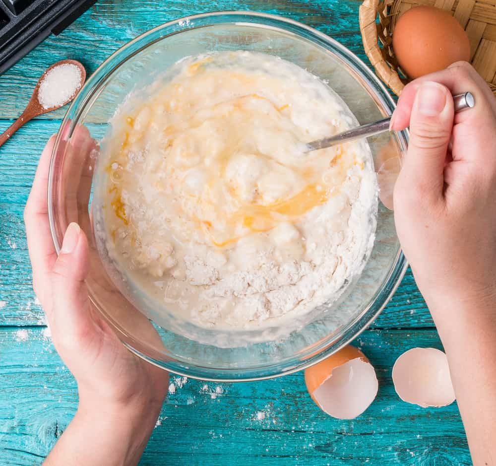 a woman mixing waffle batter in a bowl