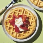 dairy free waffles on a white plate topped with sliced strawberries and dairy free whipped cream