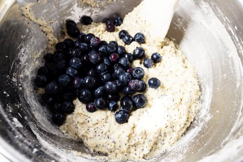 folding blueberries into muffin batter in a mixing bowl