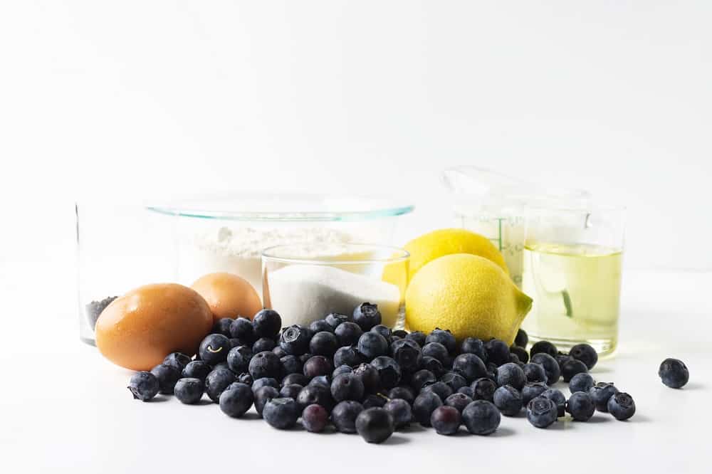 Ingredients for the recipe including blueberries, sugar, eggs, lemons, oil, and dairy free yogurt