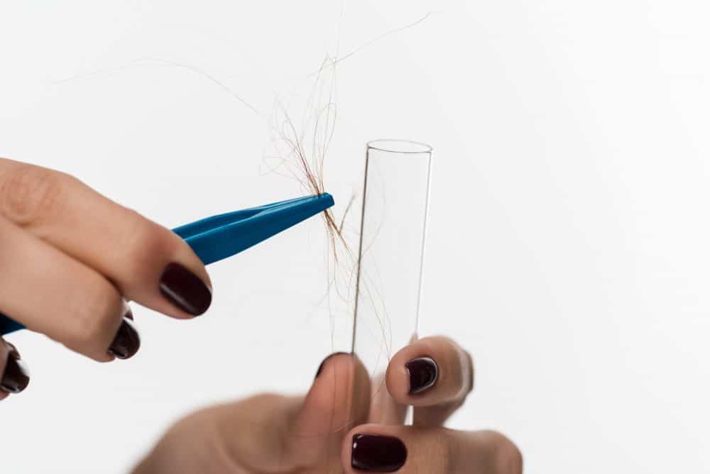 a woman holding hair with tweezers to place in a test tube