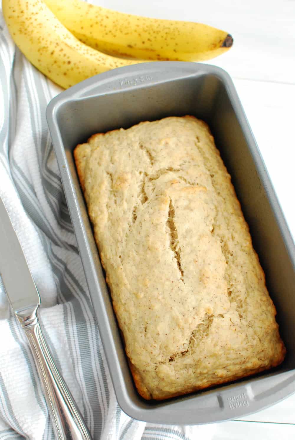 5 ingredient vegan banana bread cooked in a loaf pan, next to a knife and two bananas