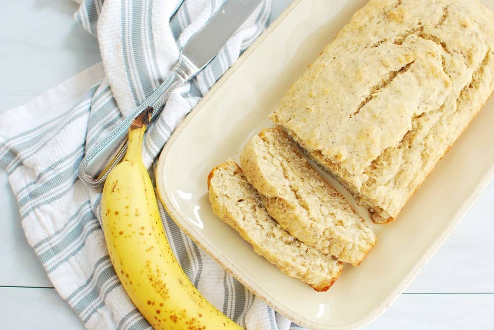 slices of banana bread on a plate, next to a napkin, banana, and knife