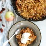 a bowl with bacon apple crisp and a spoon, next to a skillet full of the same