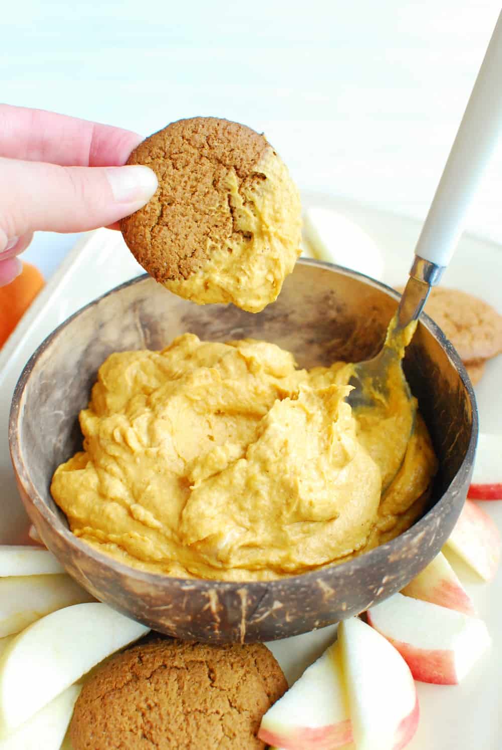 a woman dipping a gingersnap into a bowl of pumpkin dip