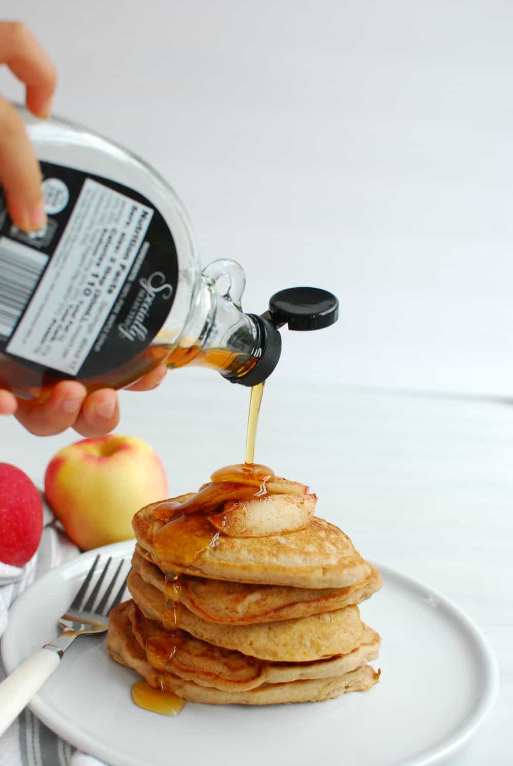 drizzling maple syrup over a stack of apple pancakes