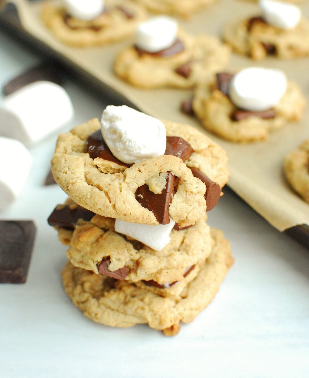 a stack of three vegan smores cookies next to some stray marshmallows and chocolate