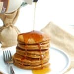 several dairy free gingerbread pancakes on a white plate with syrup being drizzled on top