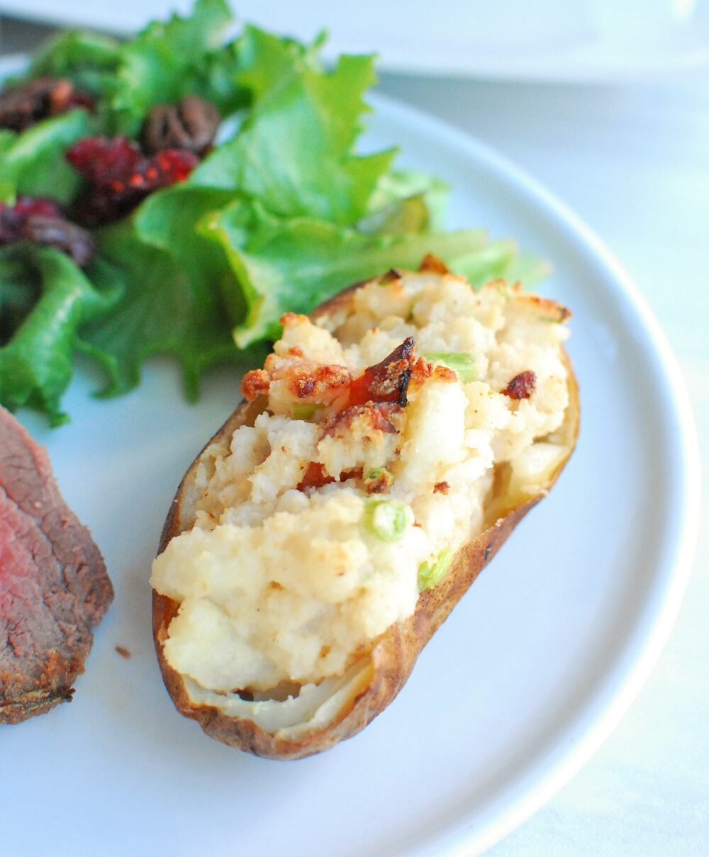 a twice baked potato on a white plate next to a piece of steak and a salad