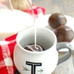 pouring milk over a dairy free hot chocolate bomb in a mug