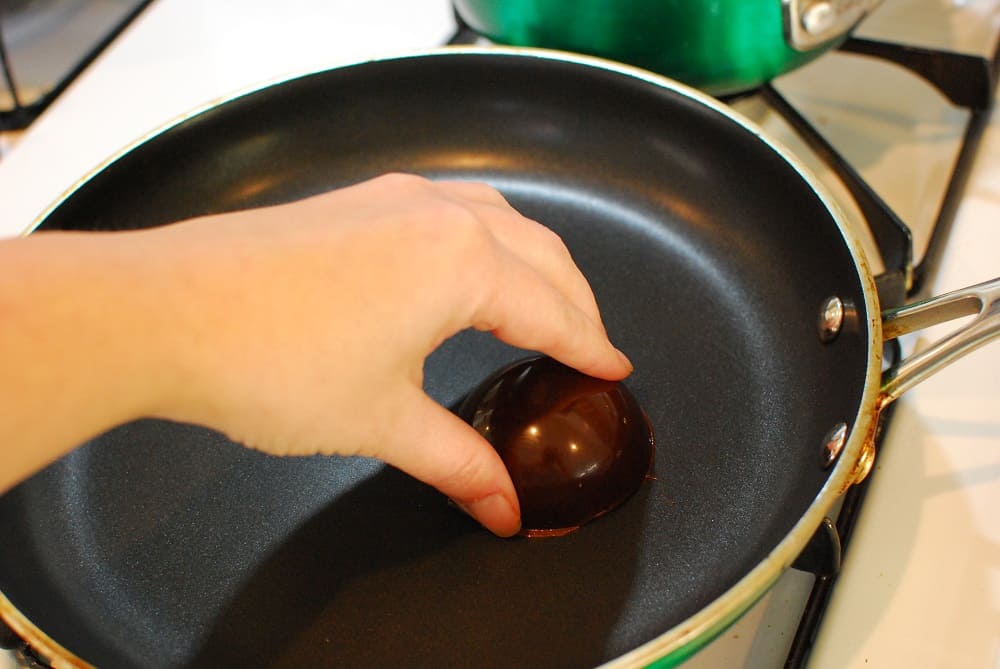 holding a chocolate dome on a warm skillet to melt the edges