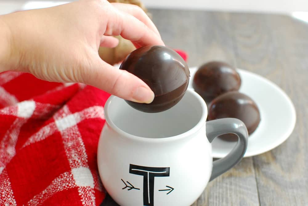 a woman's hand about to drop a dairy free hot chocolate bomb in a mug