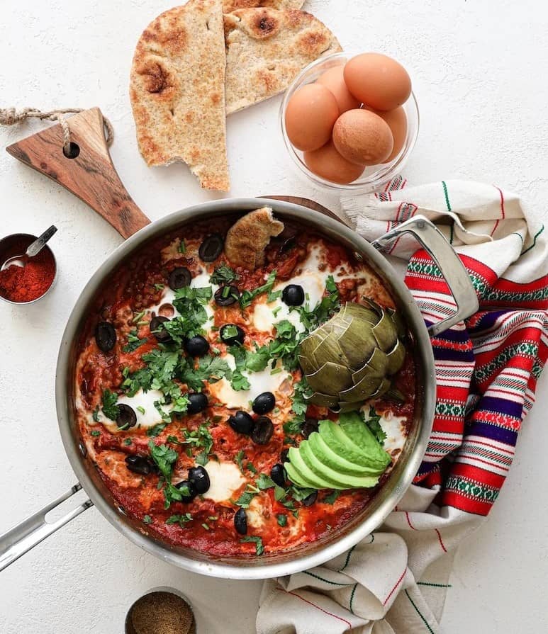 shakshuka in a skillet next to some eggs and flatbread