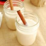 vegan coquito in a small mason jar garnished with a cinnamon stick