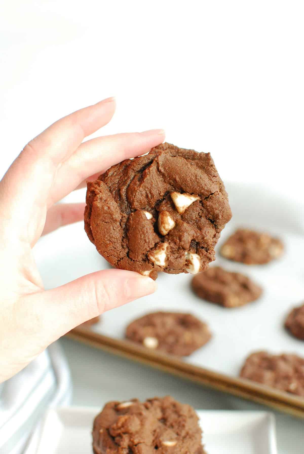 a woman's hand holding a dairy free chocolate cookie with white chocolate chips