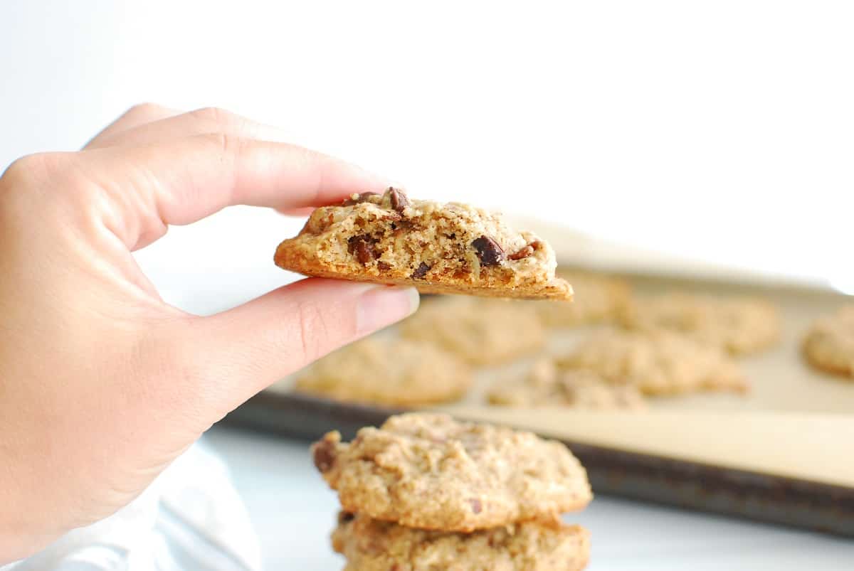 A woman's hand holding a tahini oatmeal cookie that has a bite taken out of it.