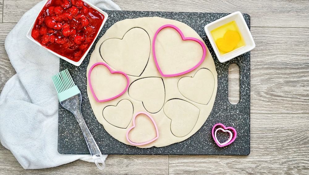 Pie crust on a cutting board with heart shaped cookie cutters.