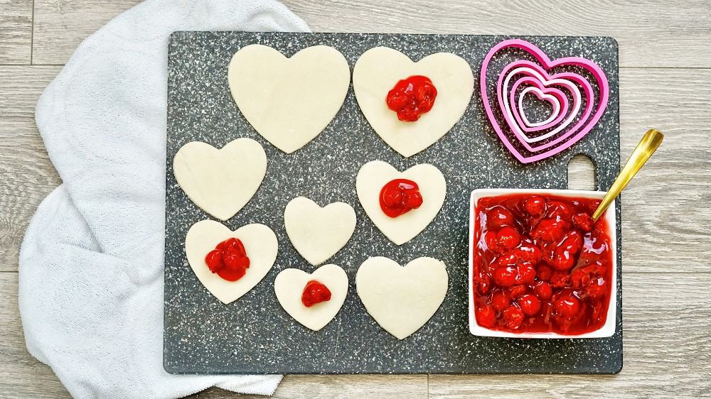 Cherry pie filling being placed in the center of pie crust shapes.