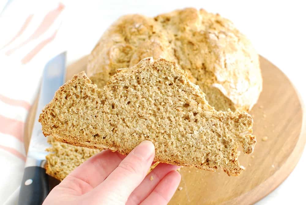 A woman's hand holding a slice of vegan Irish soda bread.