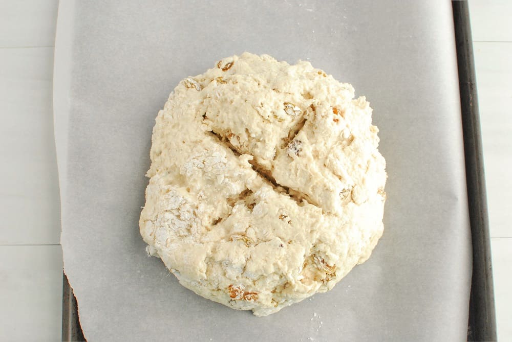 An unbaked bread dough round with an X cut in the top.