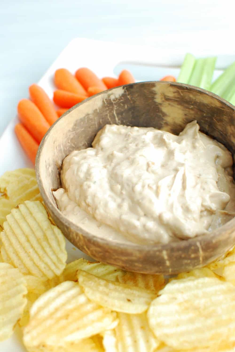 A brown bowl filled with dairy free french onion dip on a platter with chips and veggies.