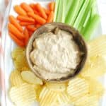 A bowl of dairy free french onion dip surrounded by potato chips, carrots, and celery.