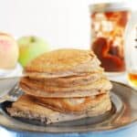 A stack of apple butter pancakes on a grey plate with some apples in the background.