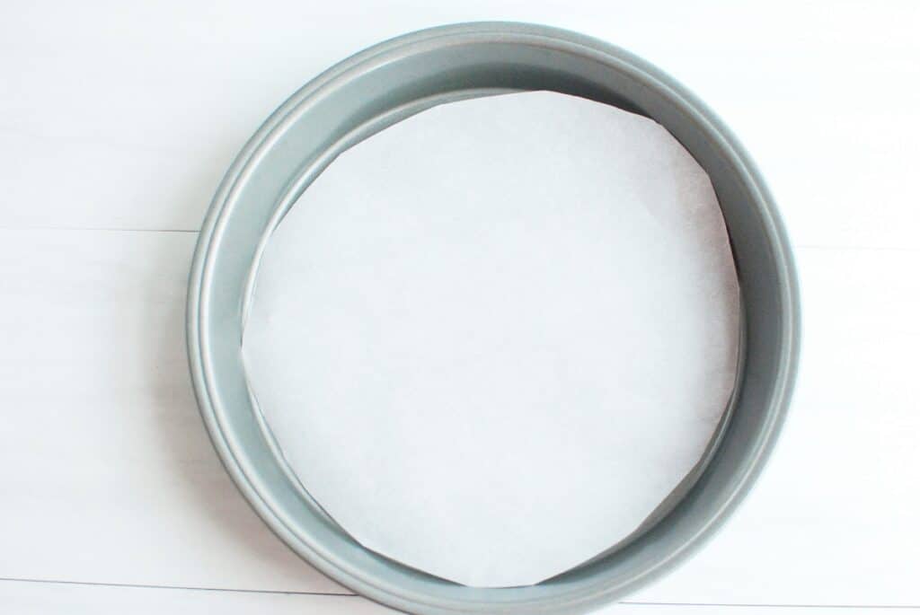 A cake pan with a circle of parchment paper in it.