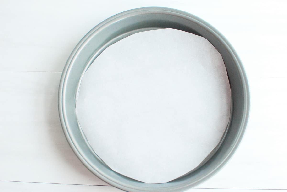 A cake pan with a circle of parchment paper in it.