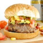 A habanero burger on a bun on a wooden serving dish with salsa falling out a bit around the edges.