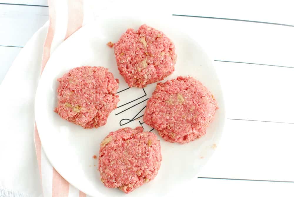 Four burger patties on a plate.