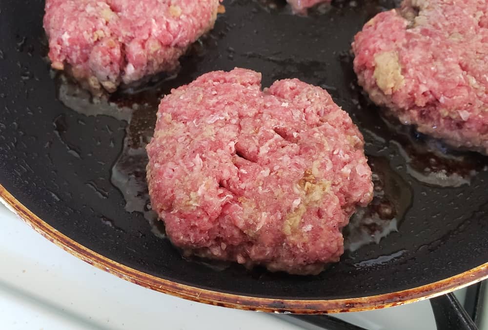 A burger cooking in a skillet.