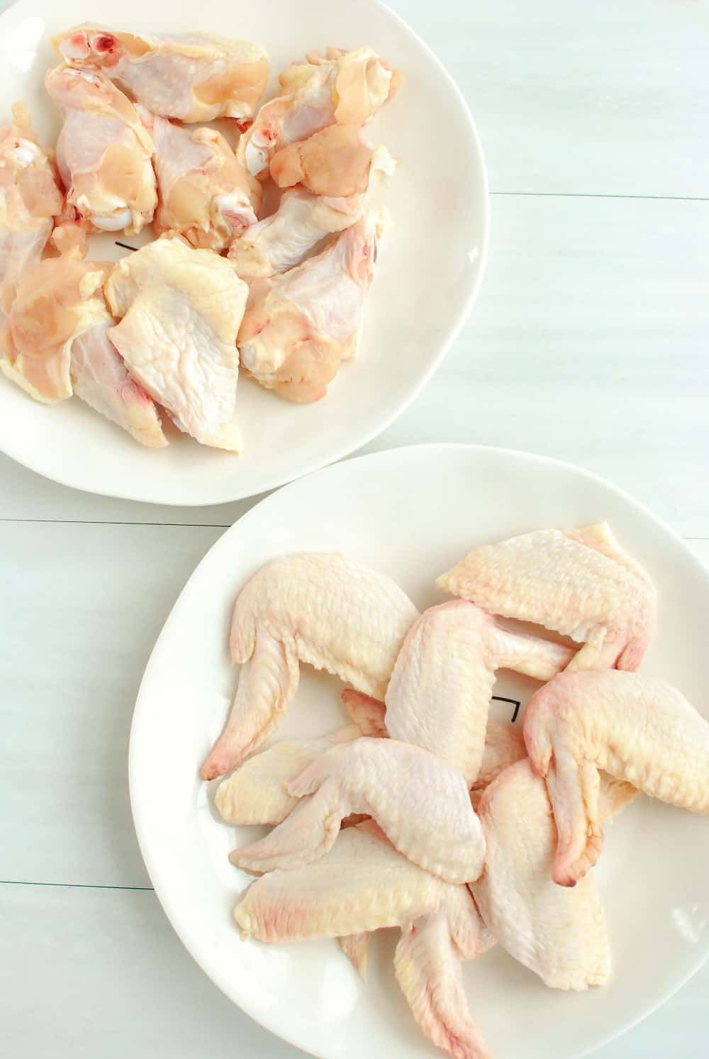 Uncooked chicken wings on white plates.