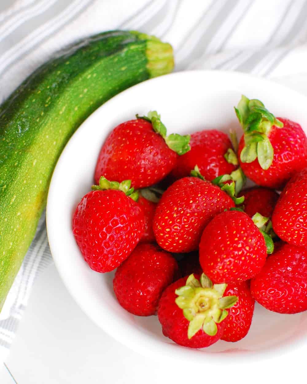 A bowl of strawberries and a zucchini.